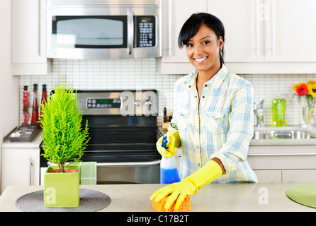 Smiling young black woman with sponge and rubber gloves cleaning kitchen Stock Photo