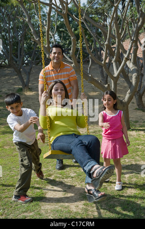 Woman swinging on a tree swing with her family pushing her Stock Photo