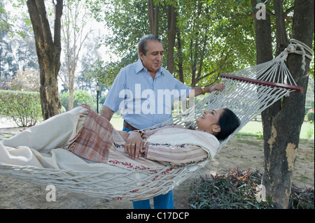 Woman in a hammock with her husband standing beside her Stock Photo