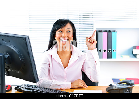 Smiling black business woman pointing up with idea at desk in office Stock Photo