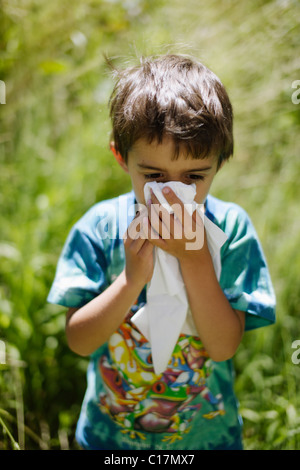 Six year old boy sneezing into tissue in garden Stock Photo