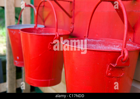 Three red painted water buckets hanging up ready to be used in case of a fire Stock Photo