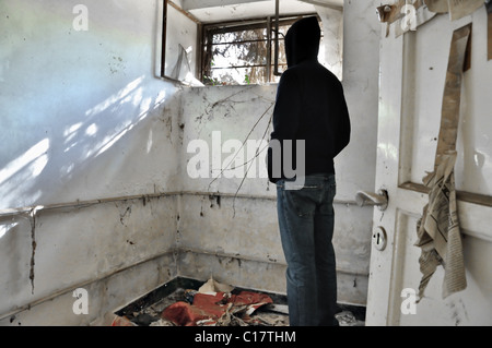Hooded man looking through the broken window of abandoned house. Stock Photo