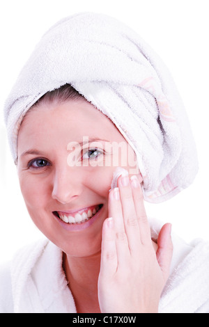 Woman with a towel wrapped around her head, putting cream on her face Stock Photo