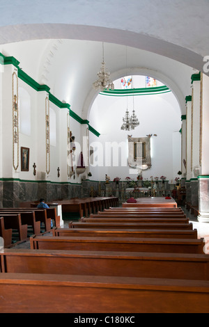 simple wood pews white plaster interior of Temple and ex‐convent of Nuestra Señora de Guadalupe with Virgen portrait above altar Stock Photo