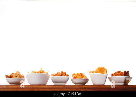 Various spiced snacks in bowls on a wooden board, crisps, peanut flips, potato sticks, roasted peanuts and potato rings Stock Photo