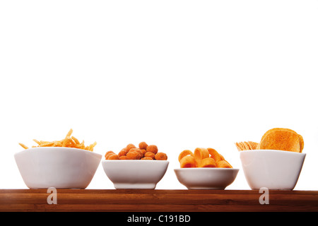 Various spiced snacks in bowls on a wooden board, crisps, peanut flips, potato sticks, roasted peanuts and potato rings Stock Photo
