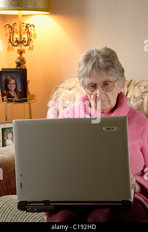 Senior lady working on her laptop computer with images of her grandchildren in background-Victoria, British Columbia, Canada. Stock Photo