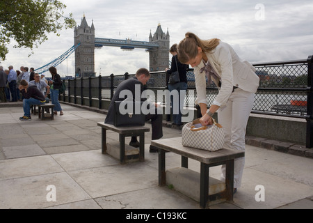 A woman in a white suit looks in her Louis Vuitton handbag on the north side of the river neat Tower Bridge. Stock Photo