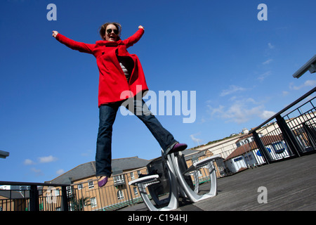 A young girl in a bright red coat pictured jumping against blue sky in Brighton, East Sussex, UK. Stock Photo