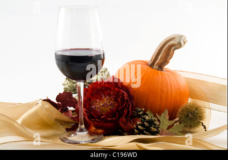 A glass of wine and pumpkin in still life with chestnut burr, pine cone, leaves, and autumn flower blossom. Stock Photo
