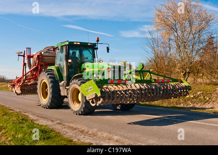 John Deere 8300 tractor and disc harrows on narrow public road - France. Stock Photo