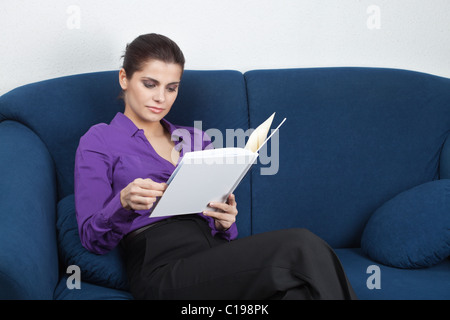 Young pretty businesswoman sitting on sofa in a waiting room and browing an album Stock Photo