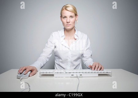 Young blond woman using a computer keyboard and mouse Stock Photo