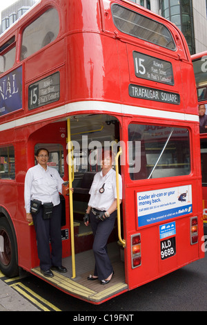 A female conductor and driver pose for a photograph on the back of the red London Routemaster bu number 15 on which they are wor Stock Photo