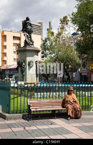 Woman wearing typical clothing sat on bench in Avanida 16 de Julio, La Paz, Bolivia, South America. Stock Photo