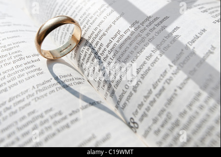 A wedding ring casting a shadow on the open pages of an open religious book Stock Photo