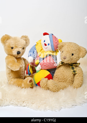 Two traditional teddy bears and a colourful toy clown sitting on a sheepskin rug. A cute celebration image for a new baby. Stock Photo