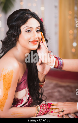 Bride's friends and family apply turmeric paste to her body as a part of Gaye Holud ceremony in Bengali Wedding Stock Photo