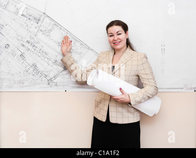 One young woman a architect standing near the big blueprint on wall and showing Stock Photo
