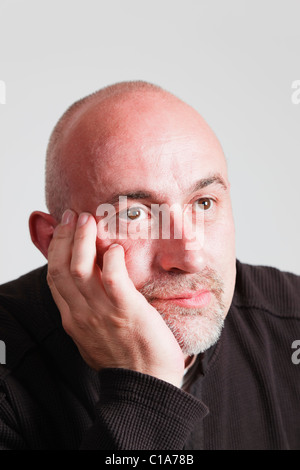 UK, Europe. Bald headed mature man resting his chin on his hand with a bored facial expression staring into the distance Stock Photo