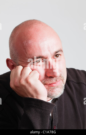 UK, Europe. Bald headed mature man resting his chin on his hand with a bored facial expression Stock Photo