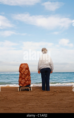 Elderly lady standing next to her shopping trolley on beach Stock Photo