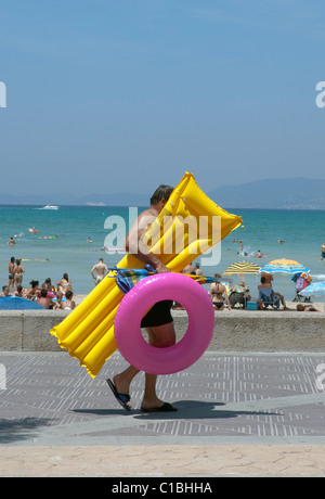 person walking seafront with air mattress and inflatable ring colorful, in Playa de Palma. Mallorca Majorca Balearic Spain Stock Photo