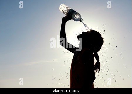 Indian girl cooling off with bottled water. India.  Silhouette Stock Photo