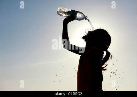 Indian girl cooling off with bottled water. India.  Silhouette Stock Photo