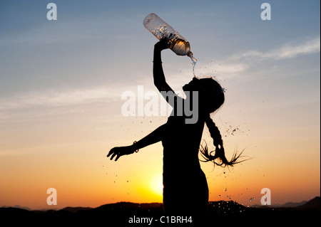 Indian girl cooling off with bottled water at sunset. India. Silhouette Stock Photo