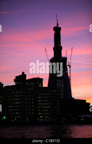 Office buildings at More London lit up at night in front of The Shard, under construction, a silhouette in the evening sunset. Stock Photo