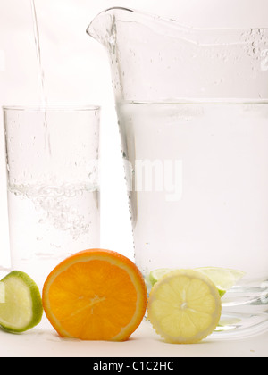 Slice of Lemon, Lime and Orange with a glass with water being poured in and a jug Stock Photo