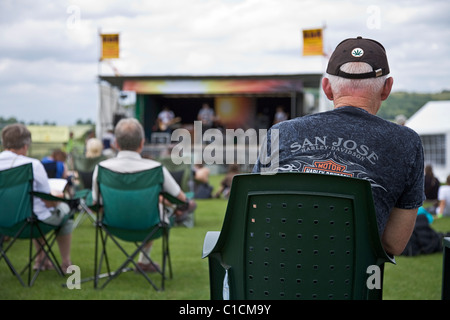 A mature male music fan wearing a baseball cap and Harley Davidson tee shirt enjoying the music at an outdoor music festival Stock Photo
