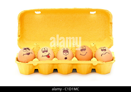 Group of fresh eggs with drawn faces depicting various emotions arranged in a cardboard egg carton against white. Stock Photo