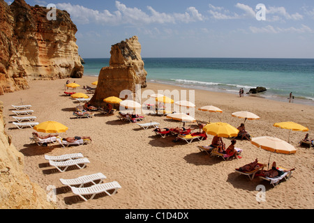 People sunbathe on the loungers under the parasols on the sandy beach. Portimao, Algarve, PORTUGAL Stock Photo