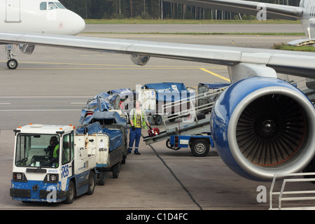 The worker of the airport puts a suitcase on a conveyor tape. Finnair. Helsinki Airport, Vantaa, FINLAND Stock Photo