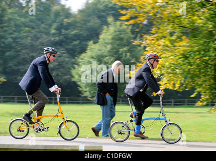 An older spectator is passed by younger competitors in the Brompton World Championships commuter bike racing in the grounds of B Stock Photo