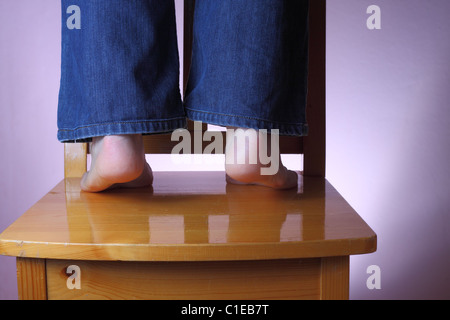 Man in jeans standing barefoot on wooden chair, keeping on his toes Stock Photo