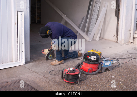 A builder using an angle grinder to cut through a concrete floor in the Uk Stock Photo