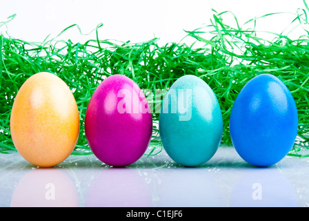 four colored Easter eggs are on a white background with Easter grass Stock Photo