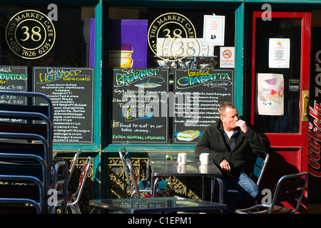 City of London Leadenhall Market Cafe restaurant snack bar young man sits at table smoking cigarette in Spring sun mugs mug chalkboard menu chairs