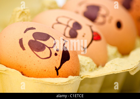 Group of fresh eggs with drawn faces depicting various emotions arranged in a cardboard egg carton against white. Stock Photo