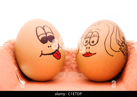 Group of fresh eggs with drawn faces depicting various emotions arranged in a cardboard egg carton against white. Stock Photo