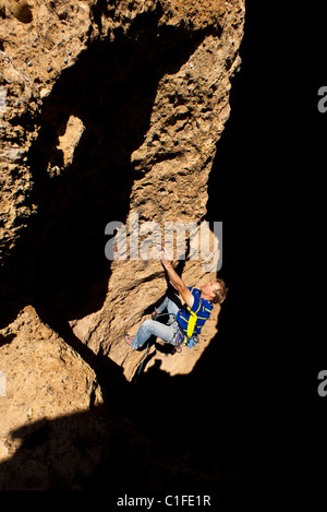 Male rock climber clings to the edge of a steep cliff as he struggles for his next grip. Stock Photo