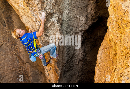 Male rock climber clings to the edge of a steep cliff as he struggles for his next grip. Stock Photo