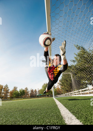 Mixed race goalkeeper in mid-air protecting goal Stock Photo