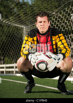 Mixed race goalkeeper crouching with soccer ball Stock Photo