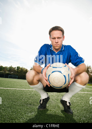 Caucasian soccer player crouching holding soccer ball Stock Photo