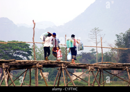 A group of Laotian people are crossing a rural river by walking on a wooden bridge in communist Laos. Stock Photo